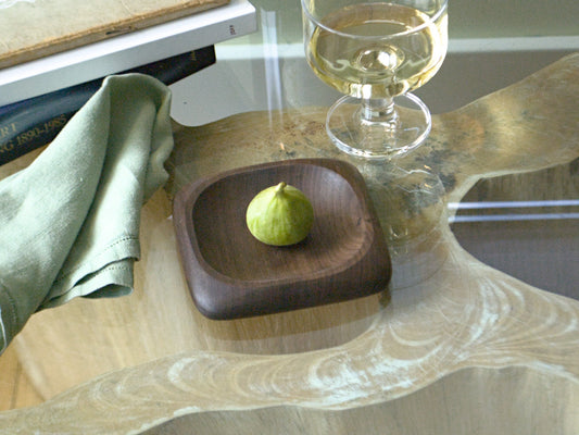Small square wooden tray with rounded edges holding a fig on a coffee table