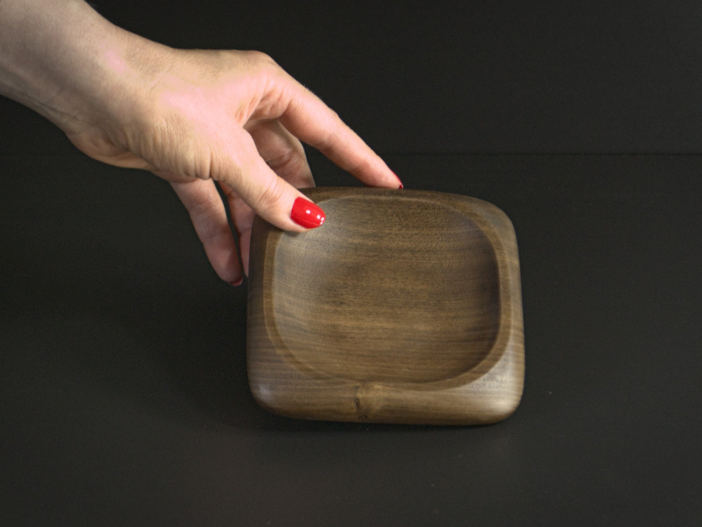 A hand holding a small square wooden tray with rounded edges